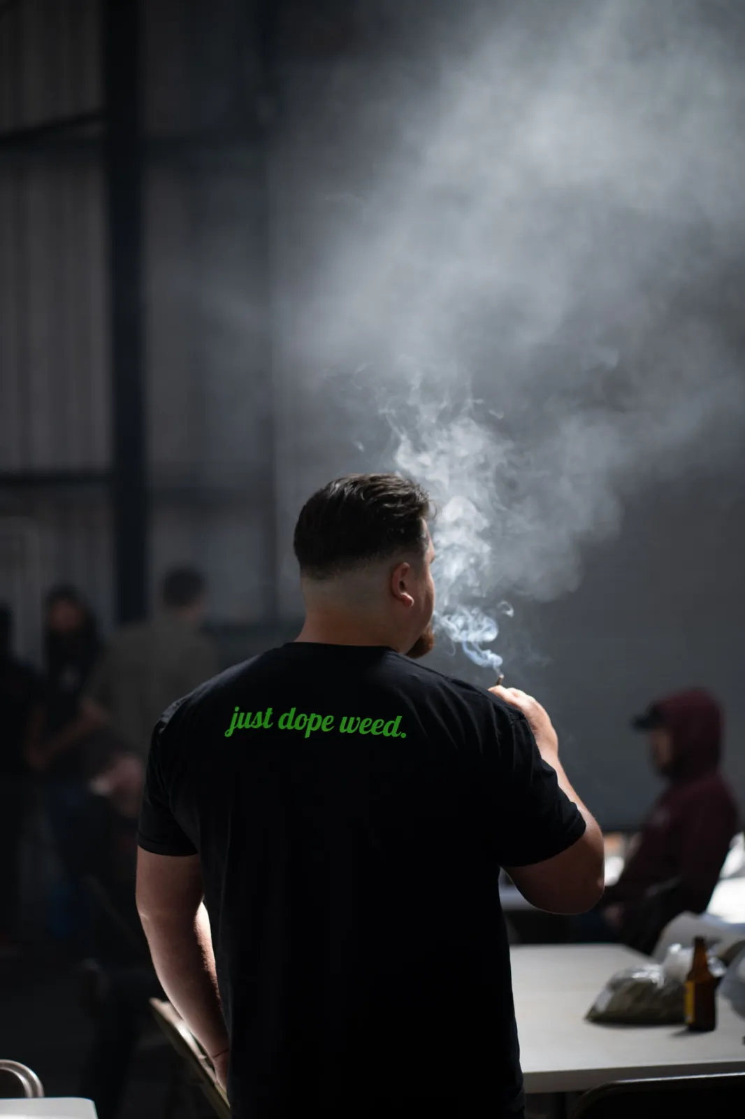 A Micro Greenz team member in a “just dope weed.” shirt, exhaling smoke