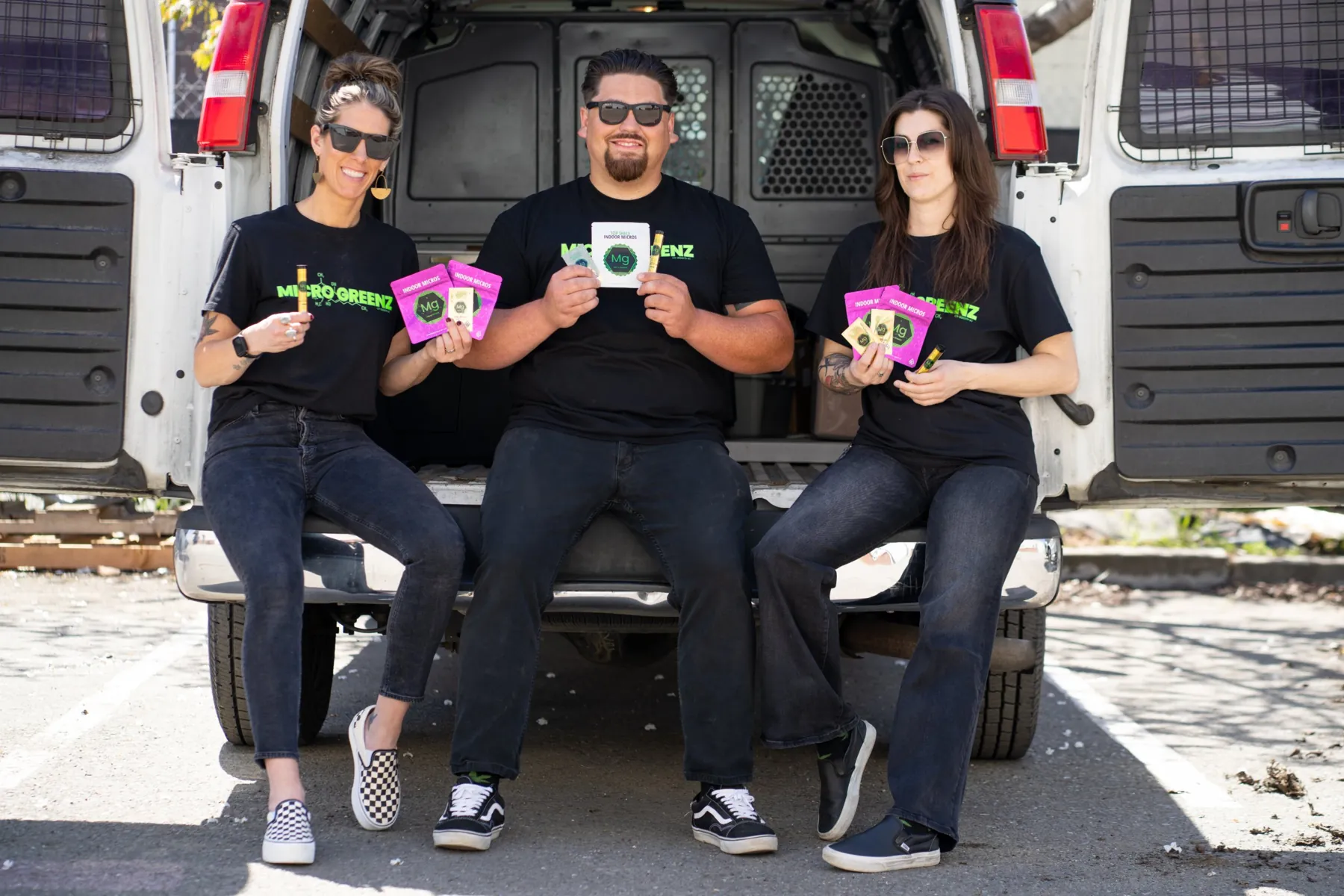 Three Micro Greenz team members sitting on the back of a white van, holding Micro Greenz products